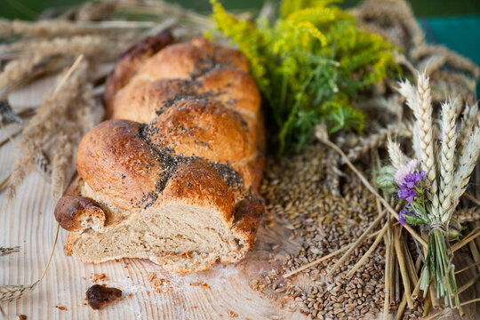 Traditional braided harvest bread loaf with poppy seeds, wheat ears, and wildflowers on a wooden board during Polish thanksgiving festival.