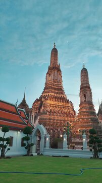 Wat Arun temple in Bangkok at sunset, golden spires of iconic Thai pagoda on Chao Phraya, historic architecture and cultural glow, 4k vertical video