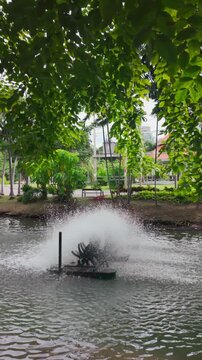 rotating water oxygen generator in park creating droplets, eco-friendly aeration device in pond producing dynamic water splashes, Lumpini park, Bangkok, 4k slow motion vertical video