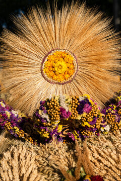 Detailed close up of a traditional harvest wreath made of wheat ears and colorful dried flowers shaping a radiating sun symbol.