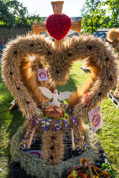 Traditional heart shaped Polish harvest wreath decorated with cereal grains, red heart, white dove, bread, and flowers outdoors.