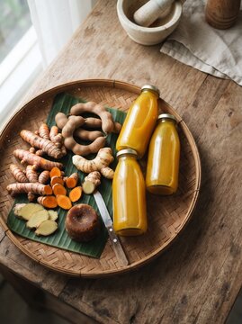 Traditional Indonesian jamu ingredients flat lay with turmeric, ginger, tamarind and herbal drink bottles on woven bamboo tray