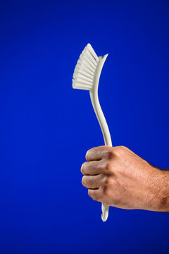 Closeup of a man's hand holding a dish cleaning brush, against a blue background.