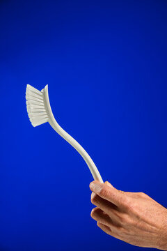 Closeup of a man's hand holding a dish cleaning brush, against a blue background.