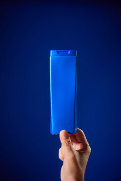 Close-up of a man's hand, against a blue background, holding a bottle of shampoo.