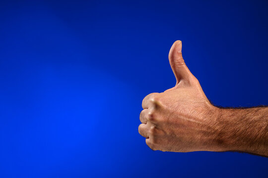 Closeup of a man's hand giving a thumbs-up and making the OK sign.