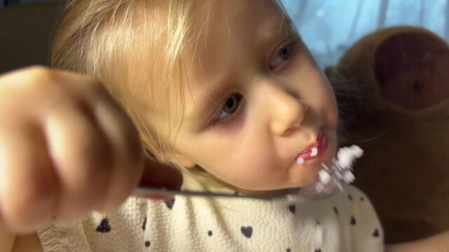 A girl eats rice from a fork and chews while looking aside in a close view, independent eating, childhood routine, everyday meal.