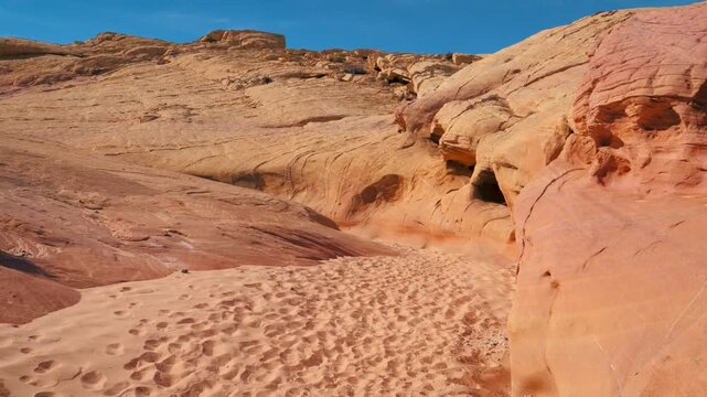 Walking through sandy desert canyon surrounded by colorful red sandstone rock formations, displaying natural erosion and unique geological layers on sunny day in nevada state. Pov hiking hiker