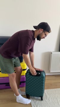 Young man removes a green suitcase from a stacked pile of colorful luggage in a room