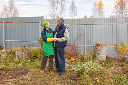 Mature couple holding hands in an autumn garden beside a metal fence. Gardening together in a backyard allotment. Outdoor partnership and companionship. Seasonal yard care and home gardening