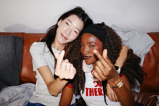 Two friends giving thumbs up gesture on couch at home
