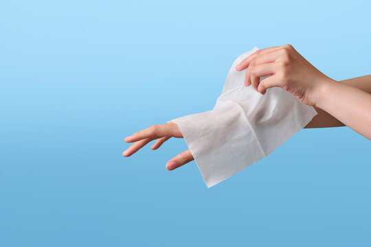 Person wiping hand with a white wet wipe against a blue background