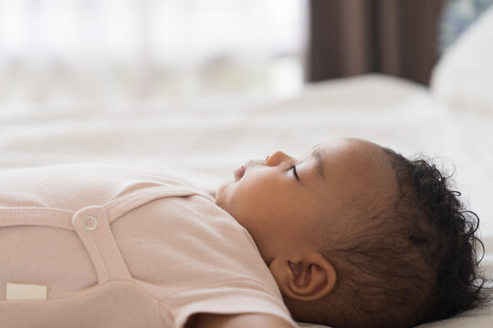 African American newborn little black baby boy taking sweet peaceful nap on soft white blanket, healthy sleep concept for innocent newborn child at home