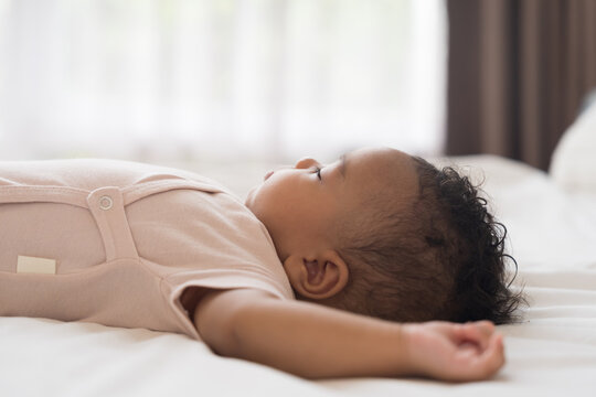 African American newborn little black baby boy taking sweet peaceful nap on soft white blanket, healthy sleep concept for innocent newborn child at home