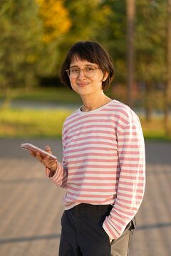 A woman pauses outdoors holding her phone at golden hour
