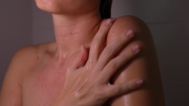 Young woman strokes her wet shoulder and collarbone in the shower, emphasizing smooth skin, hydration and a soothing body-care ritual with a fresh beauty atmosphere