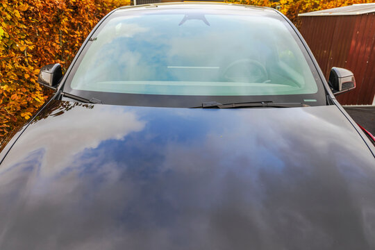 Close-up view of black car windshield, wipers and glossy hood with cloud reflections. Sweden.