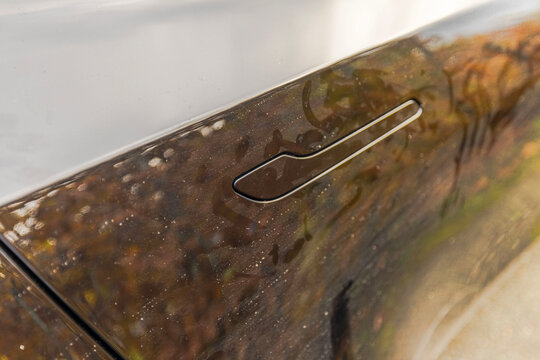 Close-up view of flush car door handle on glossy panel with reflections and visible dust. Sweden.