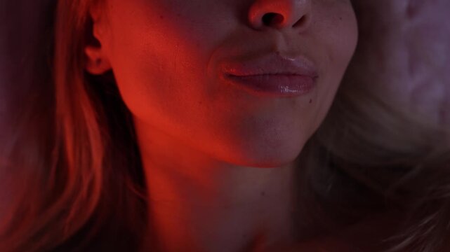 Young blonde woman bites her lip and softly purses her lips in a sensual close-up. Intimate bedroom lighting highlights desire, flirtation and passionate feminine energy