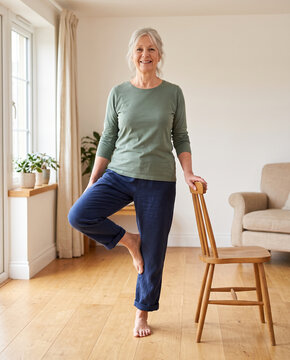 Senior woman doing a balance exercise beside a chair at home