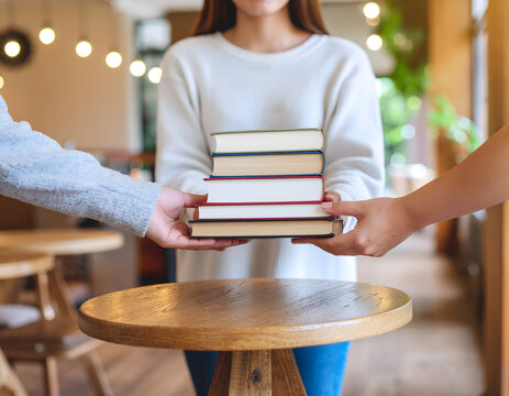Students sharing and holding a stack of hardcover books indoors