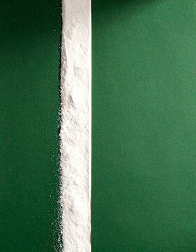 Vertical line of fine white powder between deep green panels, minimal overhead flat lay with copy space