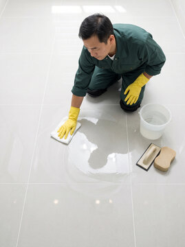 Worker cleaning tile surface with a white cloth while crouching on a glossy porcelain floor, top-down view. Precise finishing for flooring installation, grout cleanup and home maintenance