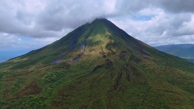 Beautiful massive, singular green rock or monolith rising out of the jungle. Grey cloud covers the top of Arenal Volcano, Costa Rica, Central America.