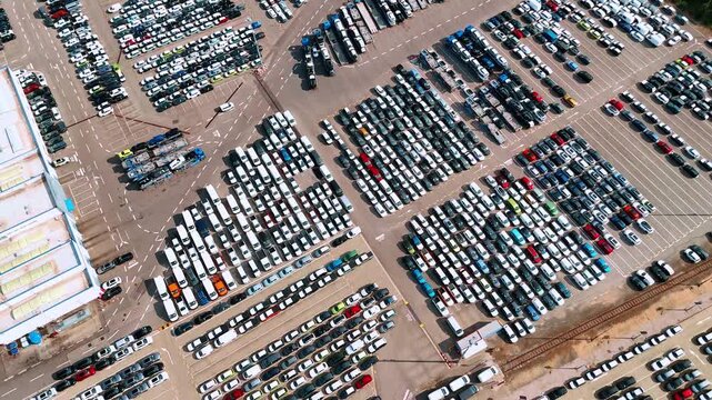 Access lanes divide car storage rows beside railway tracks. Vehicles form angled rows divided by broad access lanes beside a roof and railway tracks.
