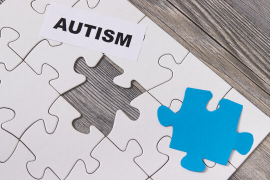 Inscription autism, white and blue puzzle as symbol of Autism Spectrum Disorder