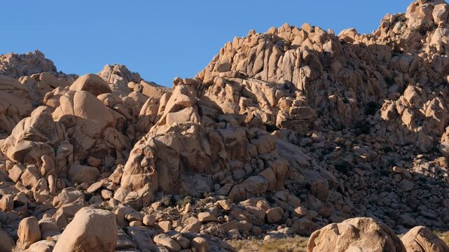 Rugged desert mountain slope covered with massive granite boulders panning under a clear blue sky, capturing the wild and arid natural landscape of joshua tree national park