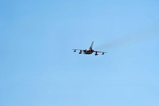 Military attack jet aircraft flying away in a clear blue sky, showing engine exhaust and tail section during flight
