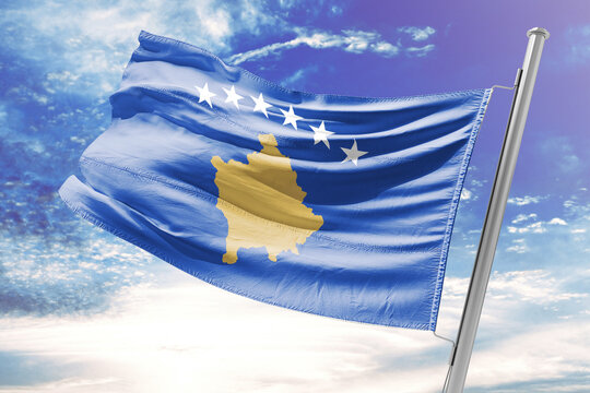 Flag of Kosovo waving in the wind against a blue sky with clouds