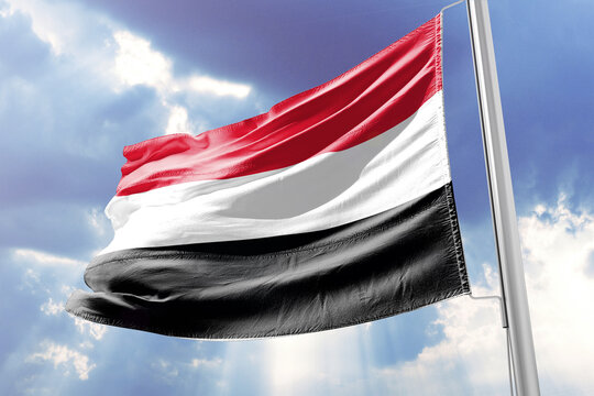 National flag of Yemen waving in the wind against a blue sky with clouds