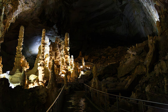 Towering stalagmites and illuminated tourist walkway in Abisso Ancona cave chamber inside Frasassi Caves, Marche, Italy. Spectacular underground limestone cave hall and karst formations