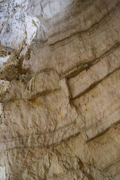 Frasassi Caves, Marche, Italy. Textured underground limestone cave wall with diagonal sedimentary layers, white calcite deposits. Natural geological backdrop for science, education, nature and travel