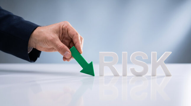 A hand places a green arrow to decrease "RISK" text, symbolizing risk reduction, strategy, and financial management, showcasing business acumen.