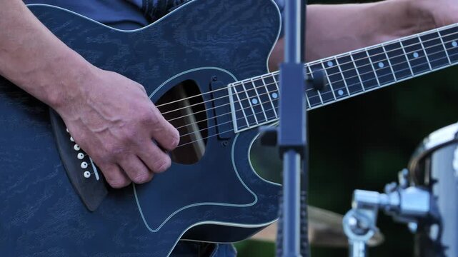 Musician strumming a blue guitar outdoors, fingers moving over the strings