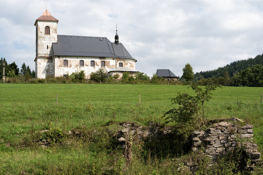 Historic church in Vrchni Orlice with stone ruins of abandoned house in foreground