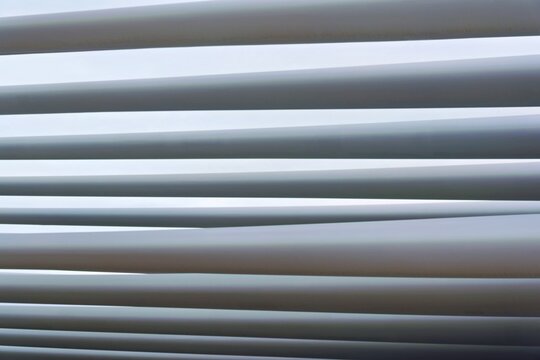 Modern architectural louvers and slats of a white pergola roof canopy provide sunshade against a bright daylight sky