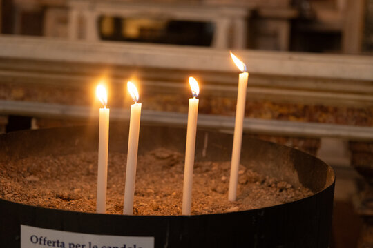 Rome, Italy - October 12, 2026: Four lit votive candles in a sand-filled holder inside a church in Rome, Italy