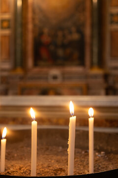 Rome, Italy - October 12, 2026: Lit votive candles in front of a blurred altar painting inside a church in Rome, Italy