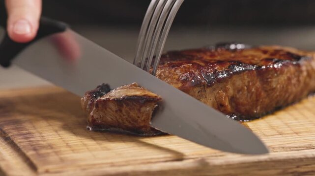 chef slices freshly cooked, juicy beef steak on wooden board in the kitchen.