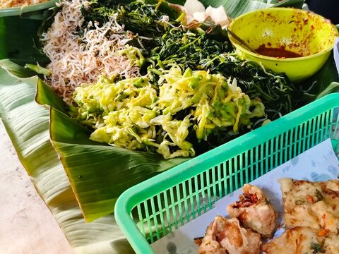 Assorted boiled vegetables with peanut sauce served on banana leaf, traditional Indonesian pecel salad and fried snacks food concept.