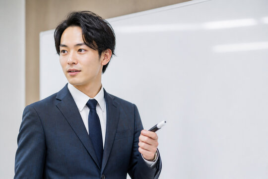 ホワイトボードの前で話すスーツ姿の日本人男性