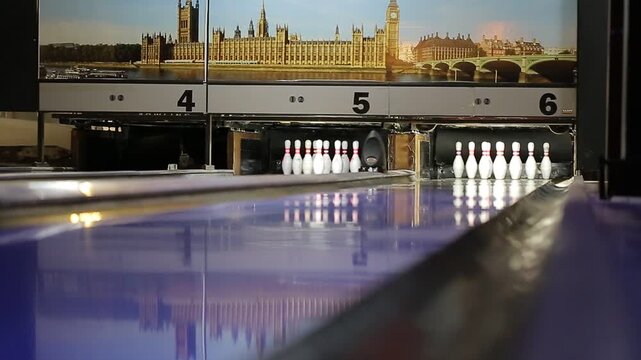 Bowling ball rolling down lane and hitting pins for successful strike inside entertainment center