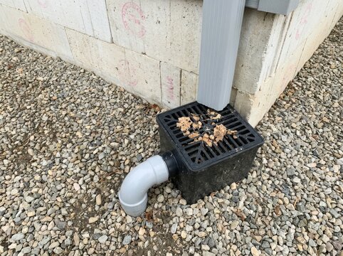 Black plastic storm drain catch basin with gravel surrounding residential foundation for underground rainwater redirection.