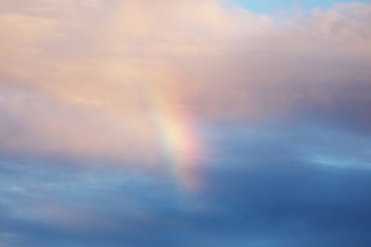Soft rainbow fragment in sky with clouds sunset background