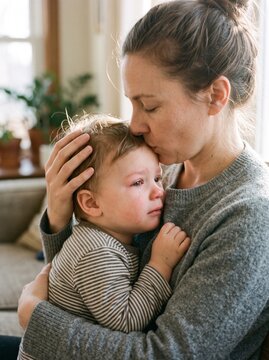 Mother kissing toddler's forehead while comforting at home  