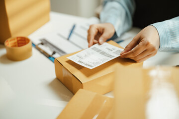 Obraz na płótnie Canvas Shipping logistics and labeling for fulfillment delivery show two hands applying a generic label to a sealed parcel, with packing tape and a clipboard behind the closeup scene for delivery.